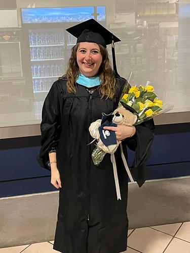 A woman wearing graduate regalia stands holding a bouquet. 