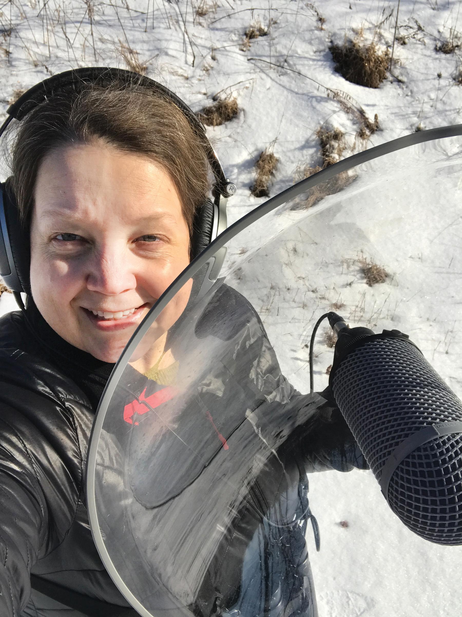 Julia Plummer holds up a parabolic microphone while wearing headphones