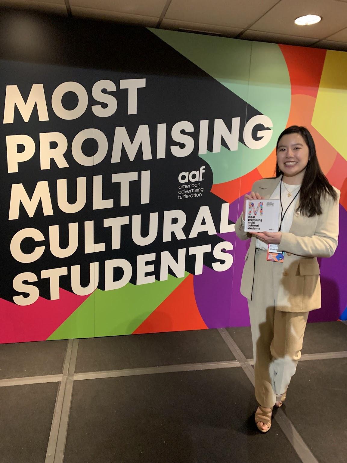 Emma Chan holding an award and posing in front of a backdrop that says most promising multicultural students