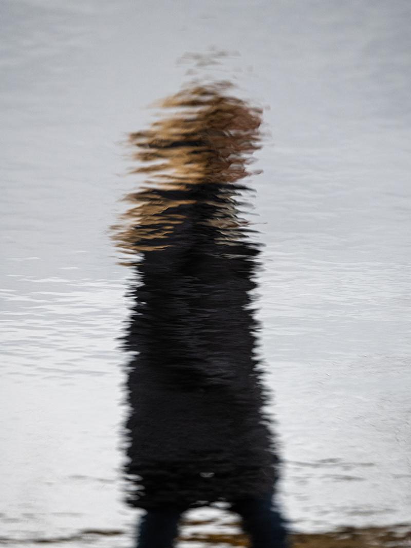 The figure of a person is reflected in a pond.