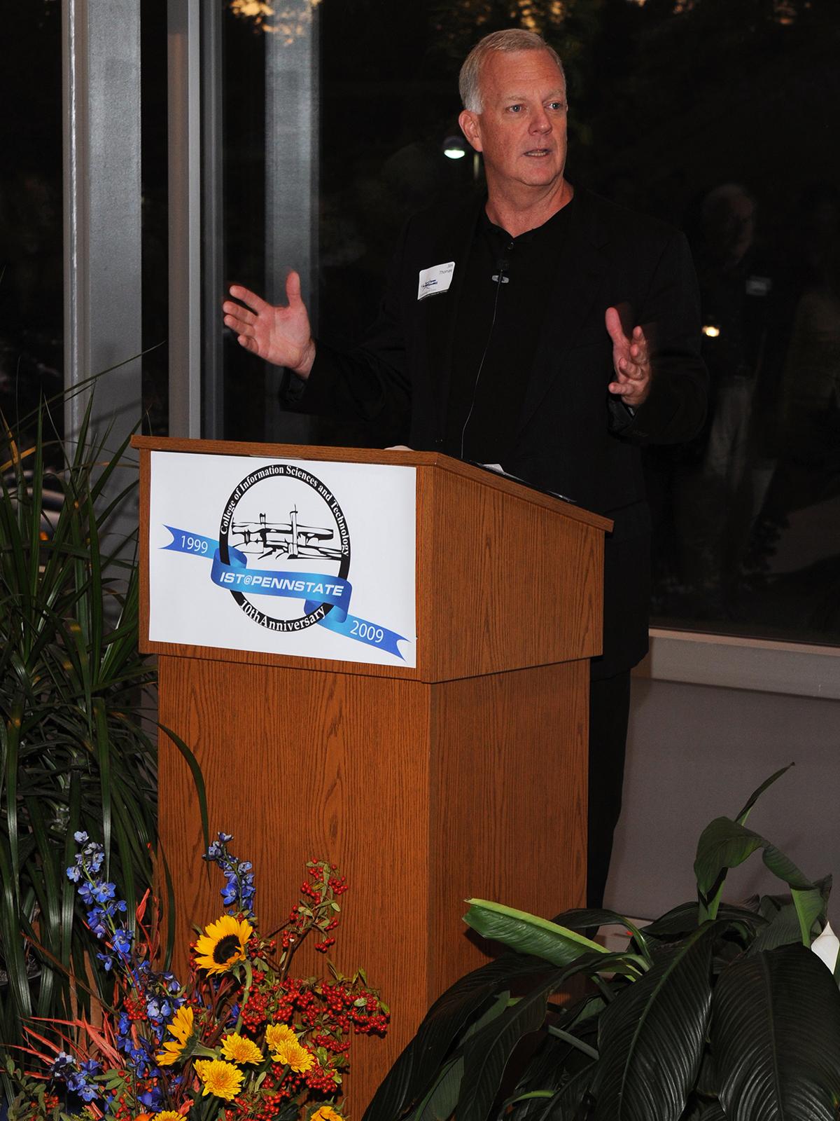 A photo of Jim Thomas standing at a lectern