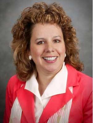 Woman with long, curly light brown hair in a pink blazer with white collared shirt underneath.