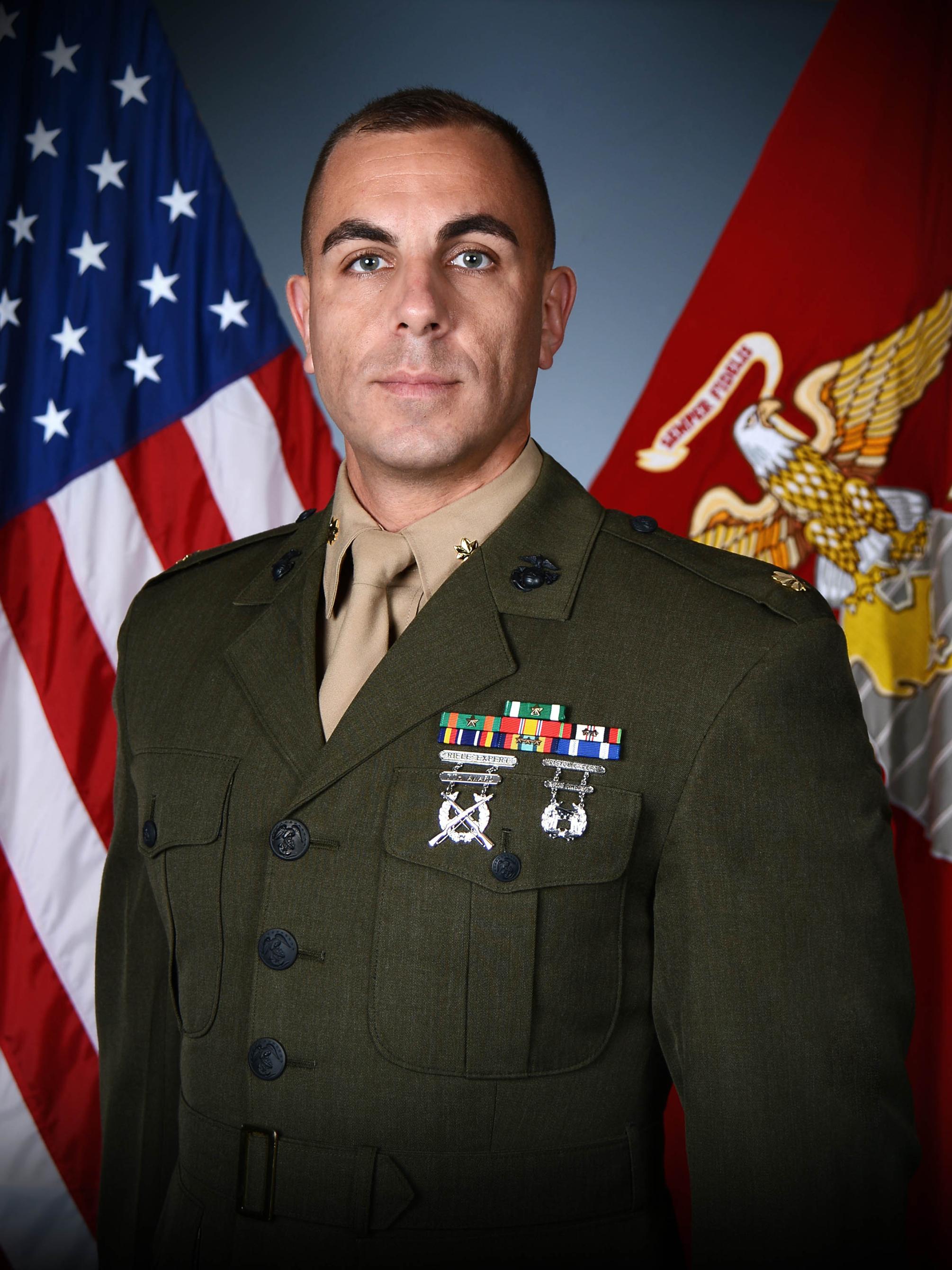 Maj. Andrew Budzien in his military uniform with a U.S. flag and a Marine Corps flag in the background