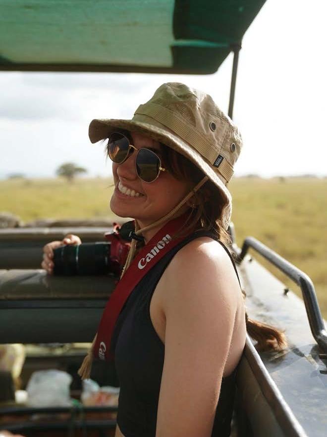 A woman, smiling, with a camera, in an open vehicle on the plains