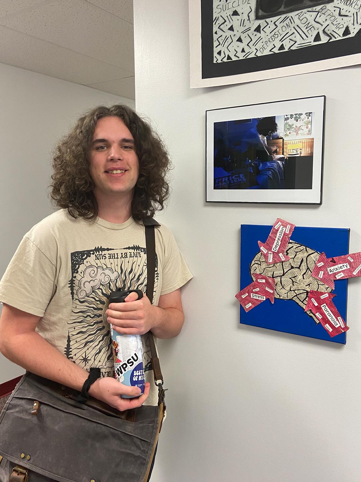Student standing in front of artwork on a wall.