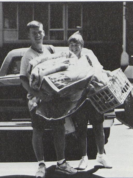A male student and a female relative wear smiles while carrying belongings on move-in day