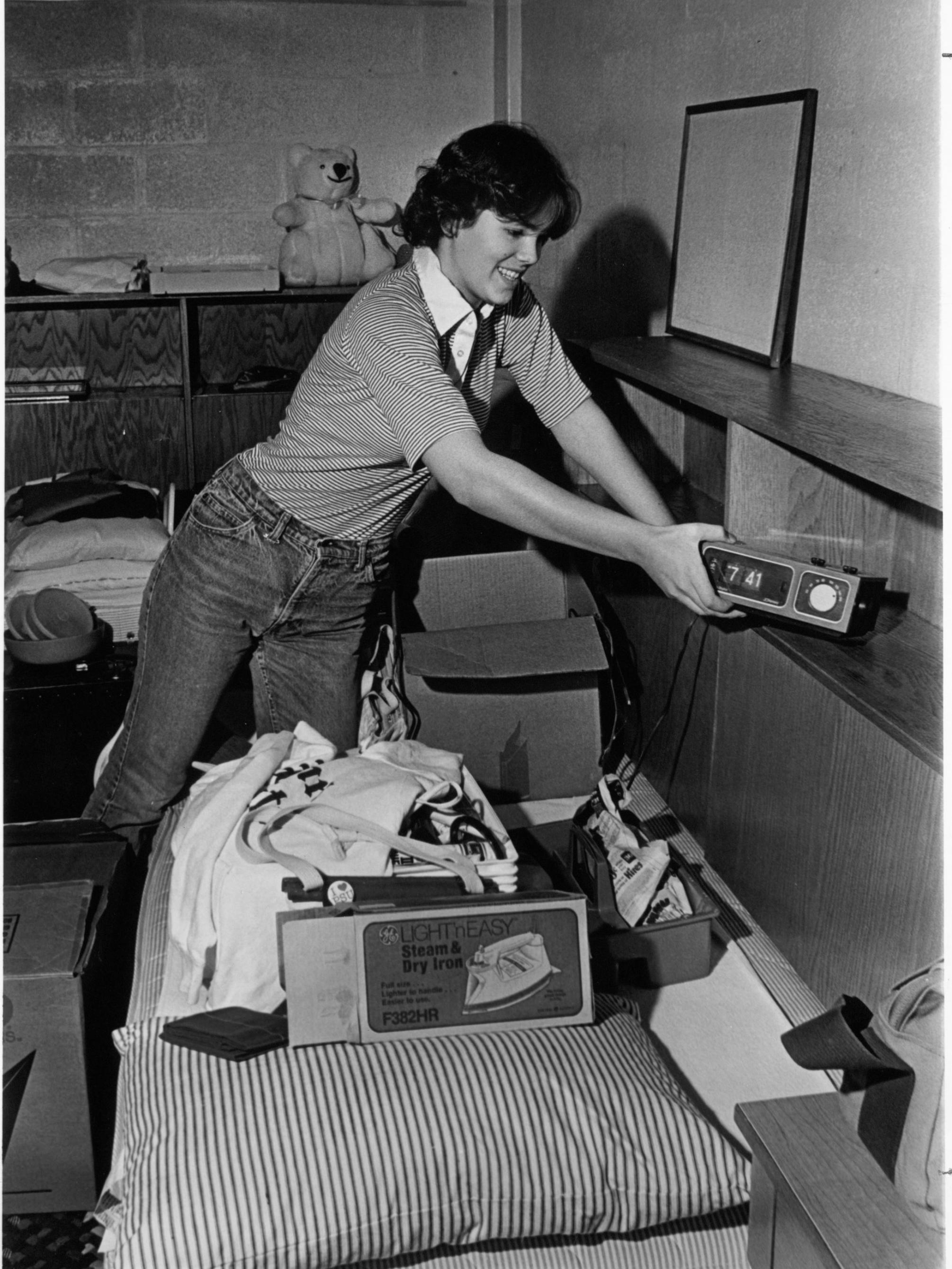 A student unpacks an alarm clock and places it on a shelf in dorm room