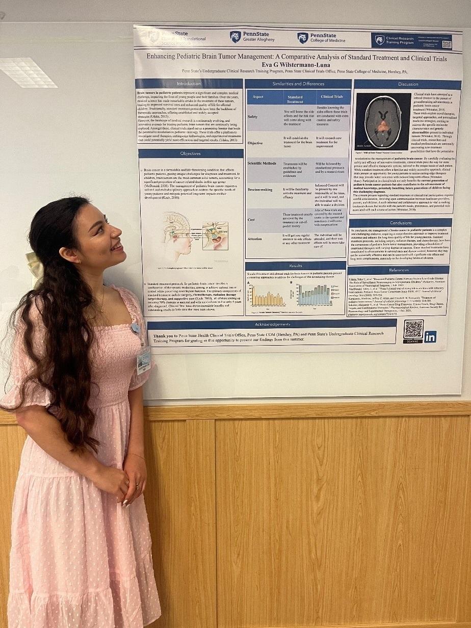 A woman stands to the left of a poster describing her experience in a clinical research internship program.