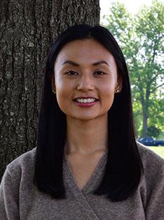 A woman stands in front of a tree.