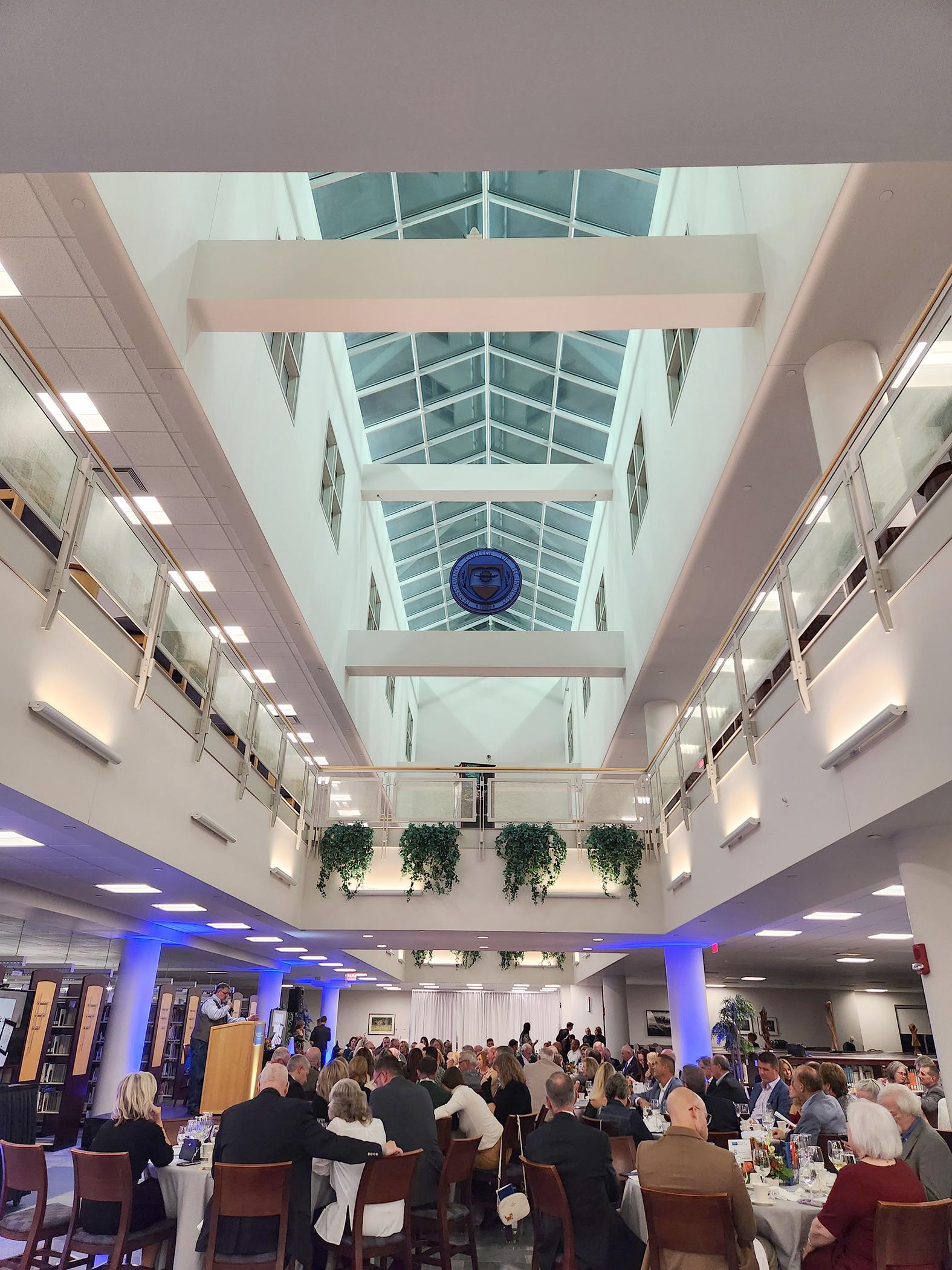 A view of the glass atrium ceiling of Madigan Library with a crowd mingling below
