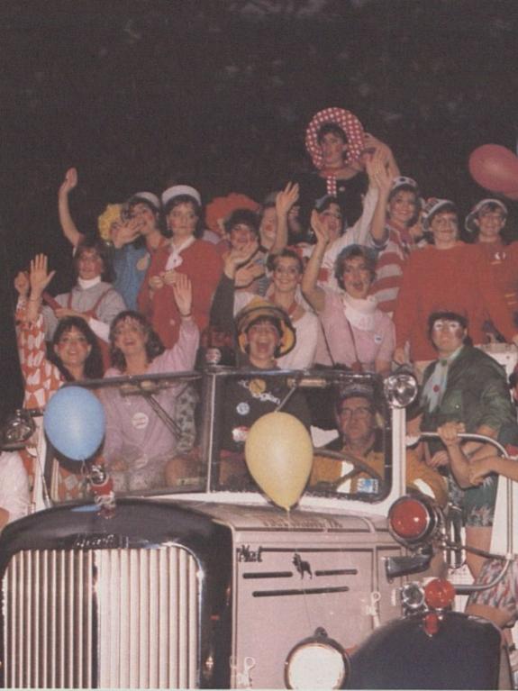 A group of students ride in a convertible in the 1984 Homecoming parade