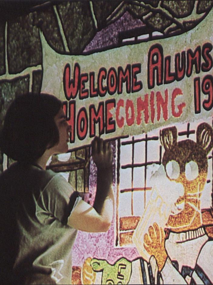 A student paints a sign that says "Welcome alums Homecoming 1971"