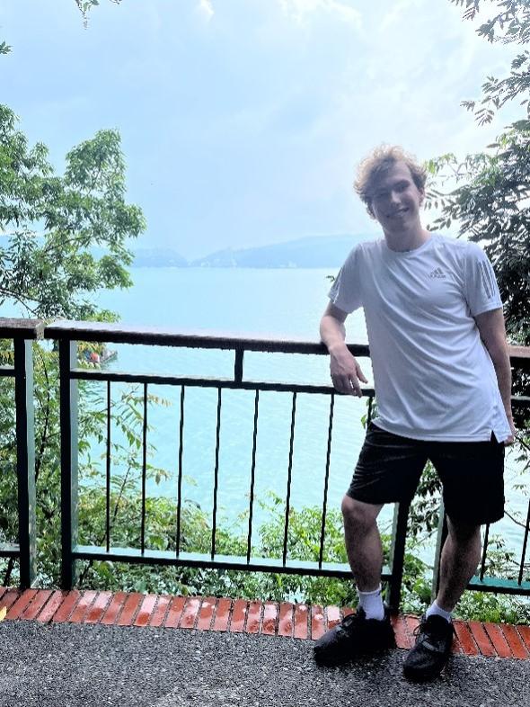 A young man standing by a fence in front of a lake