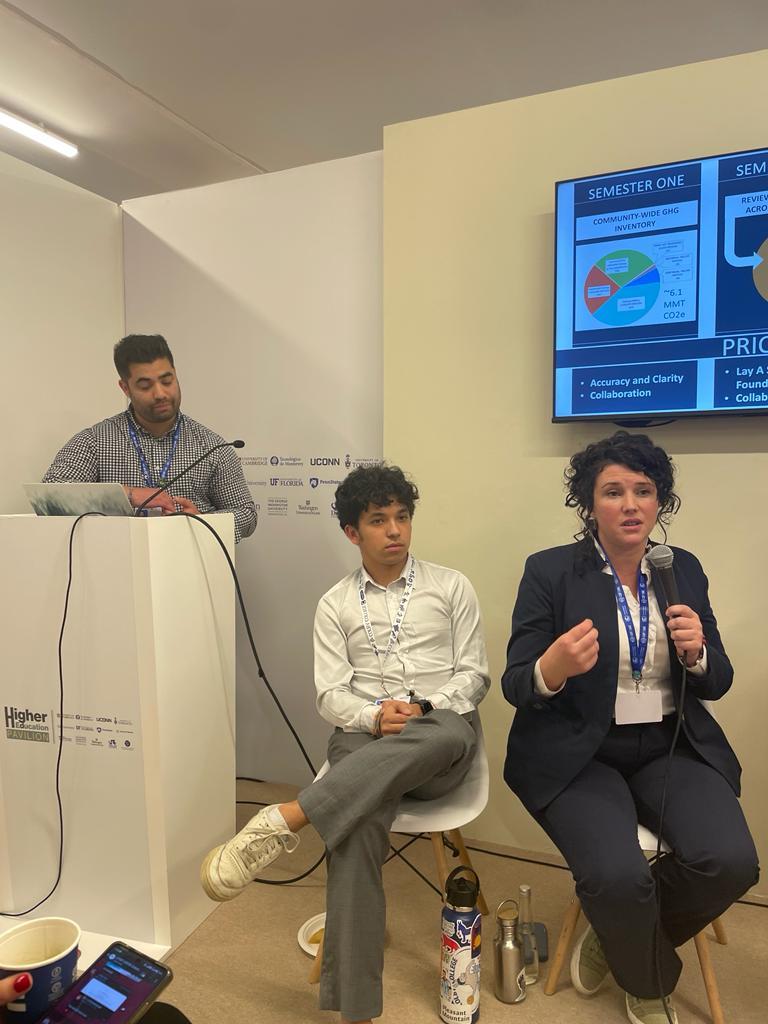 Olivia McMahon holds a microphone and gives a presentation with two people two her left