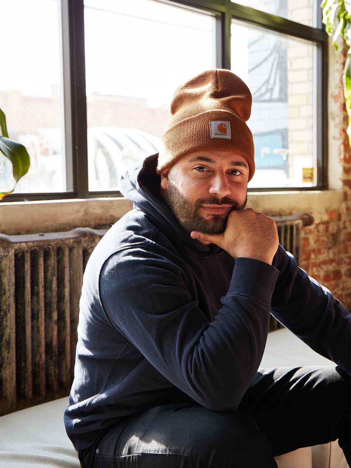Man with a hat smiling, sitting on a sofa.