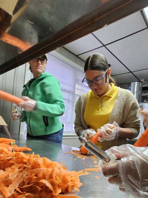 Group of people chopping carrots on a silver chopping table.