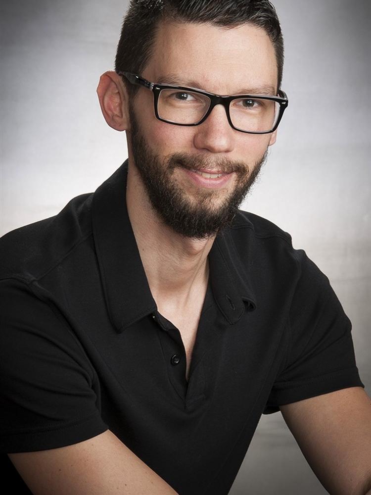 Man in glasses and black polo shirt posing for a photo