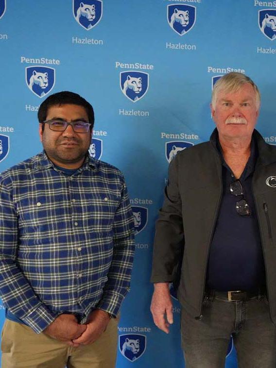 Two men standing in front of light blue Penn State Hazleton backdrop.