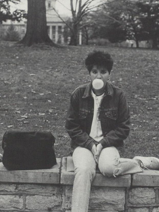 A student blows a bubble with gum while sitting on a stone wall
