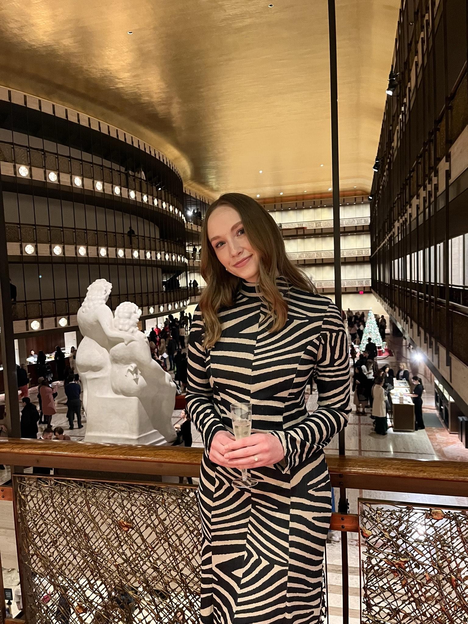 A woman wears a zebra-striped dress and leans against a contempory balcony railing.