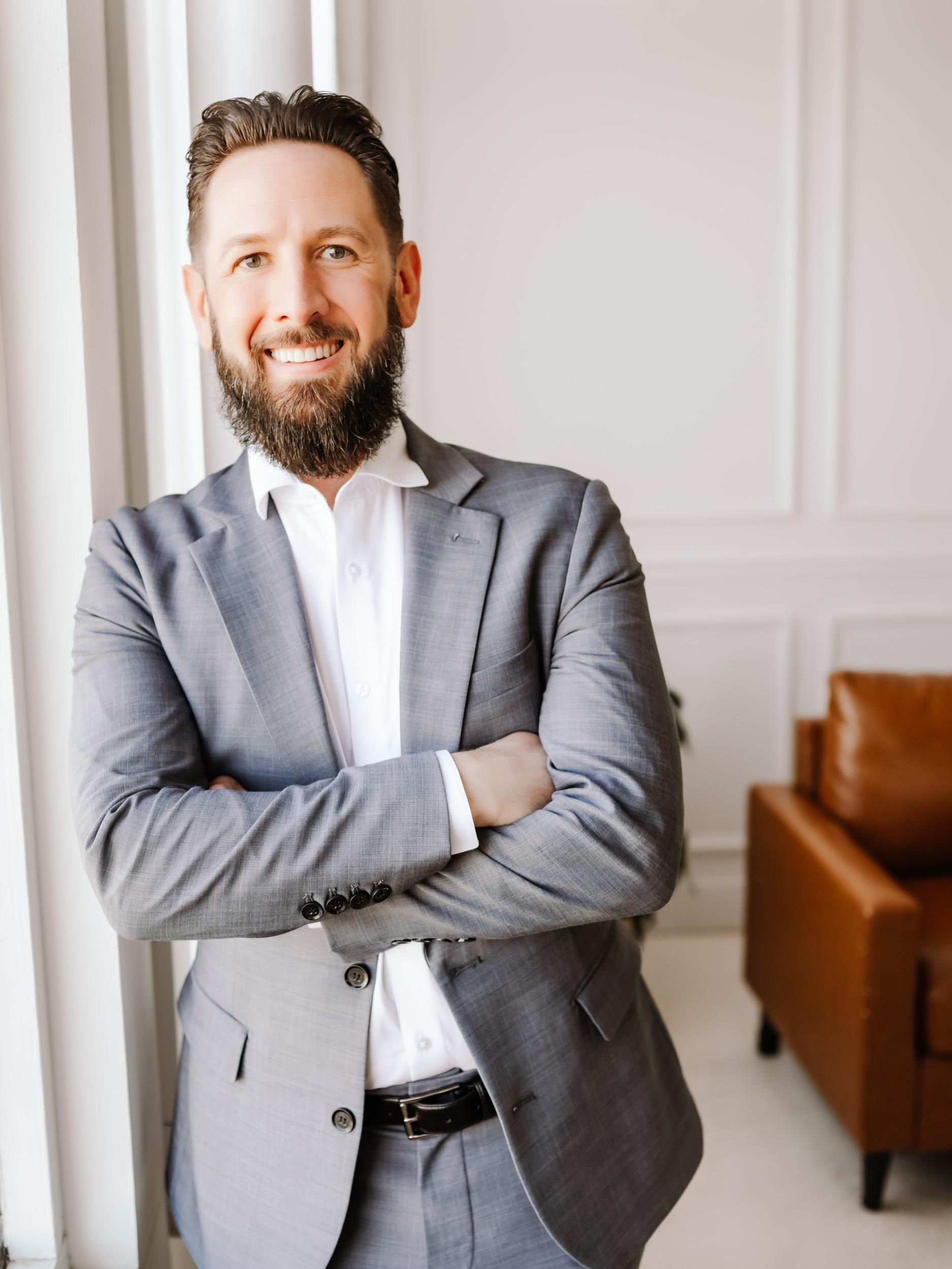 A man wearing a suit crosses his arms and leans against a wall.