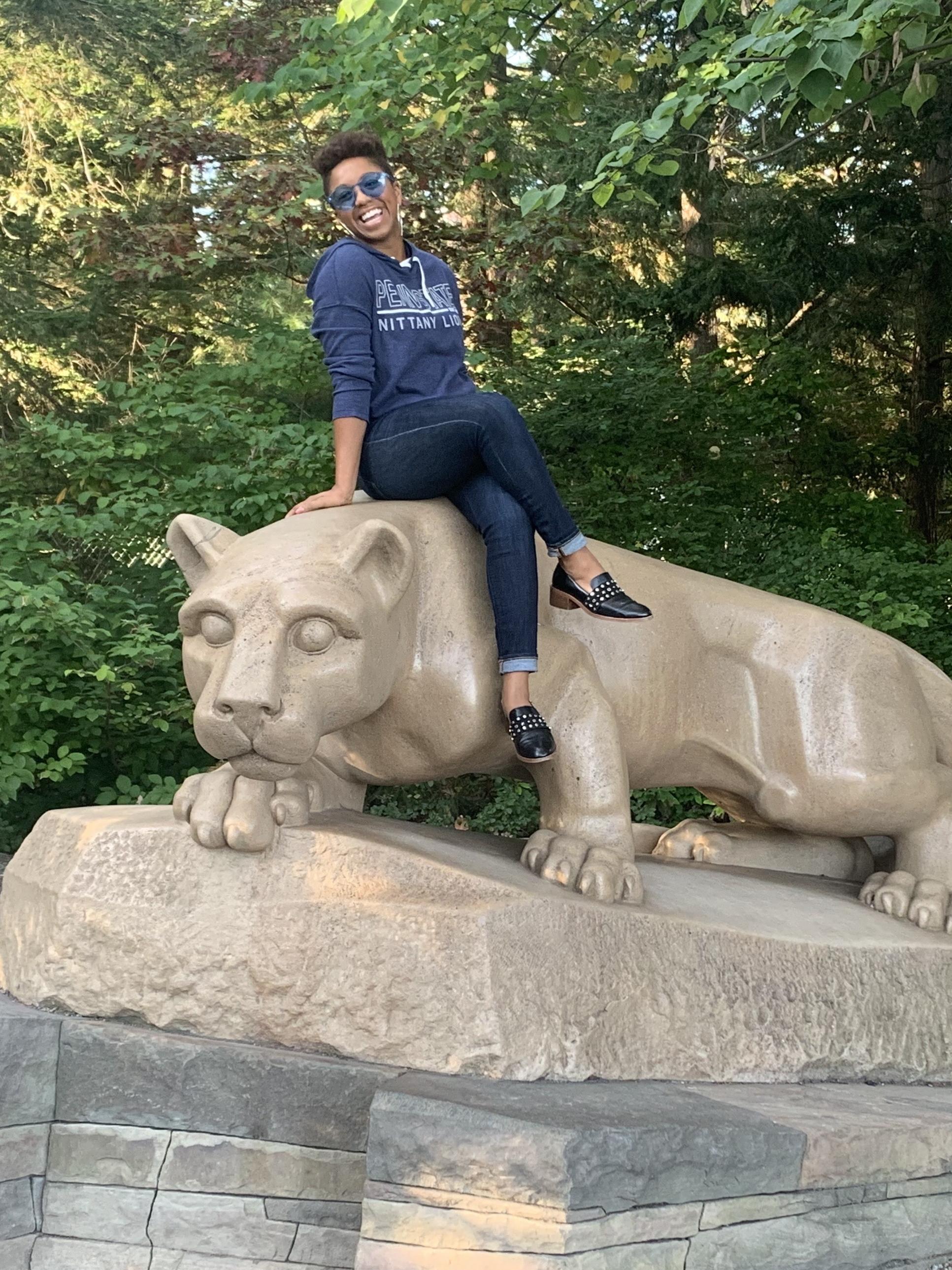 A woman of color sits atop the Nittany Lion statue.