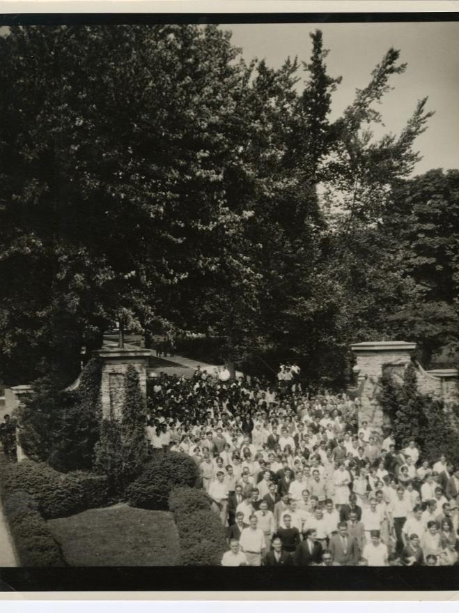 A large group of people walk through a stone gateway