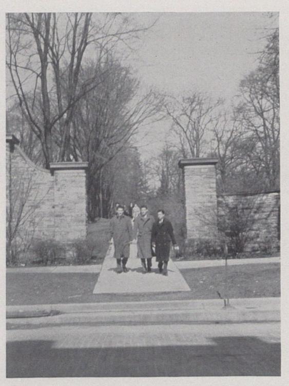Three individuals exit campus through stone gates