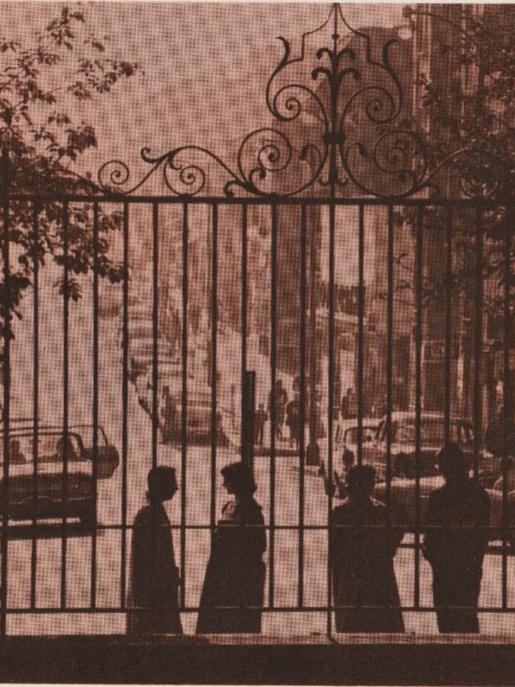 Four individuals stand behind the iron grill of the Memorial Gateway