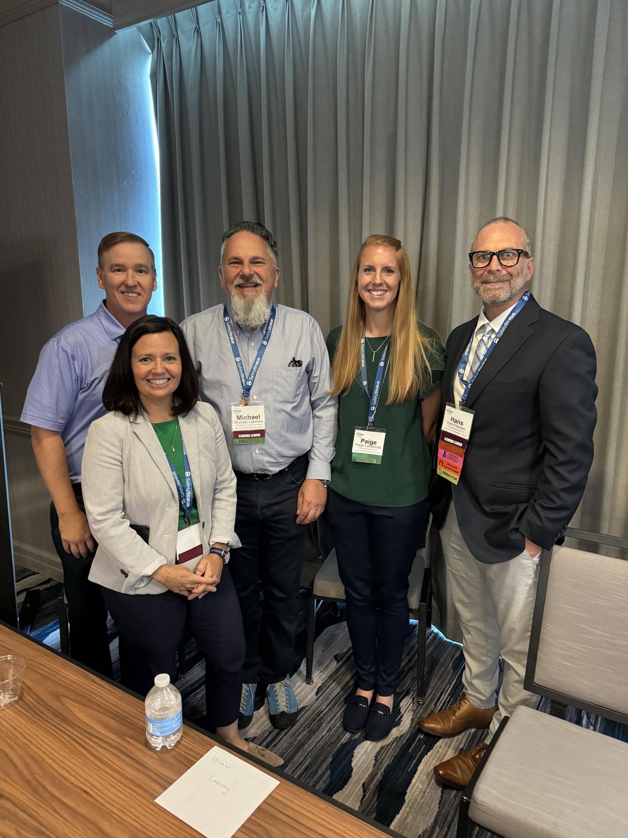 Five people smiling while attending a conference