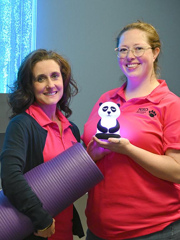 A woman at left holds a yoga mat while a woman at right holds a light-up panda.