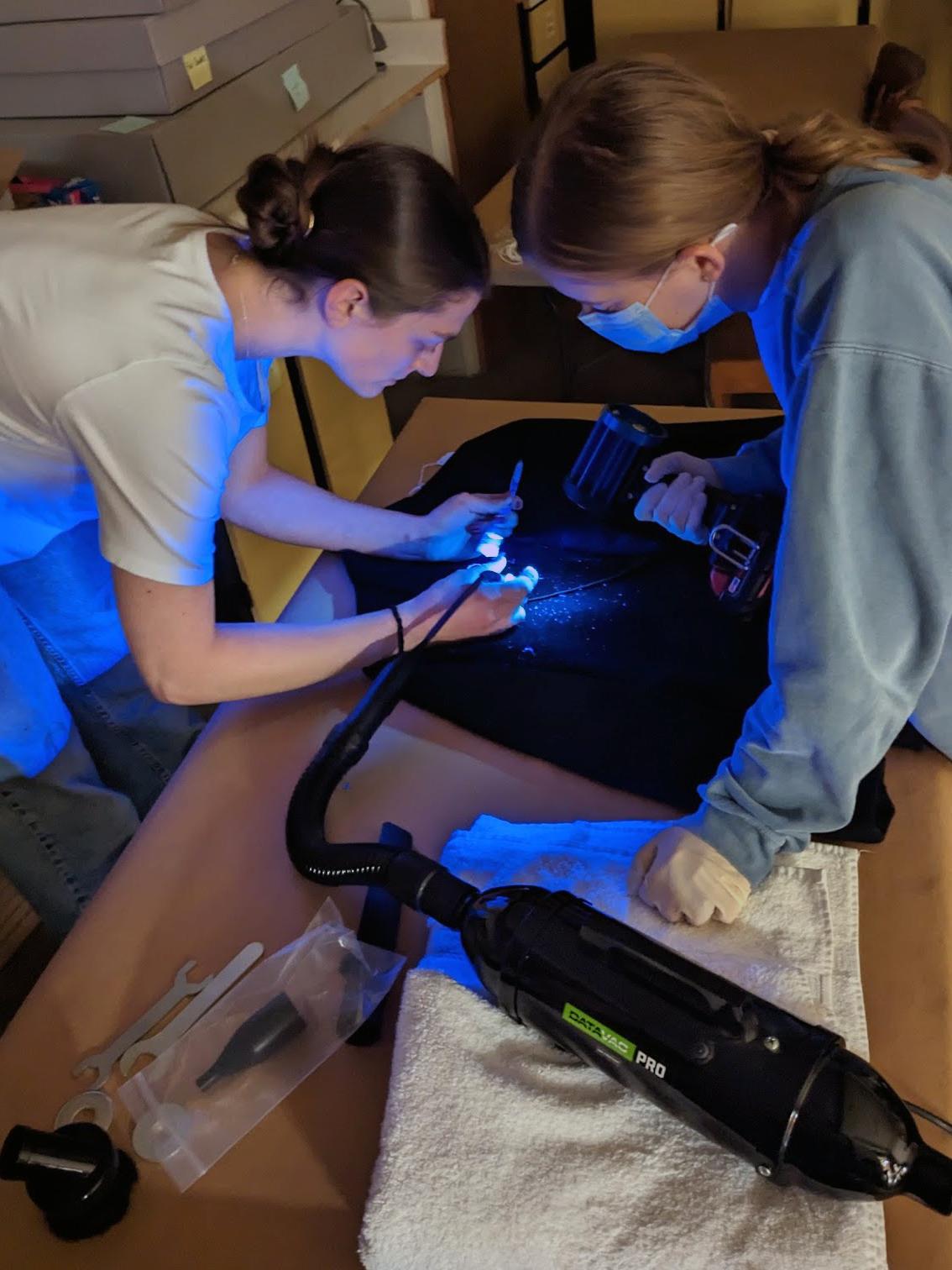 Two women lean over a garment with UV lights and additional equipment