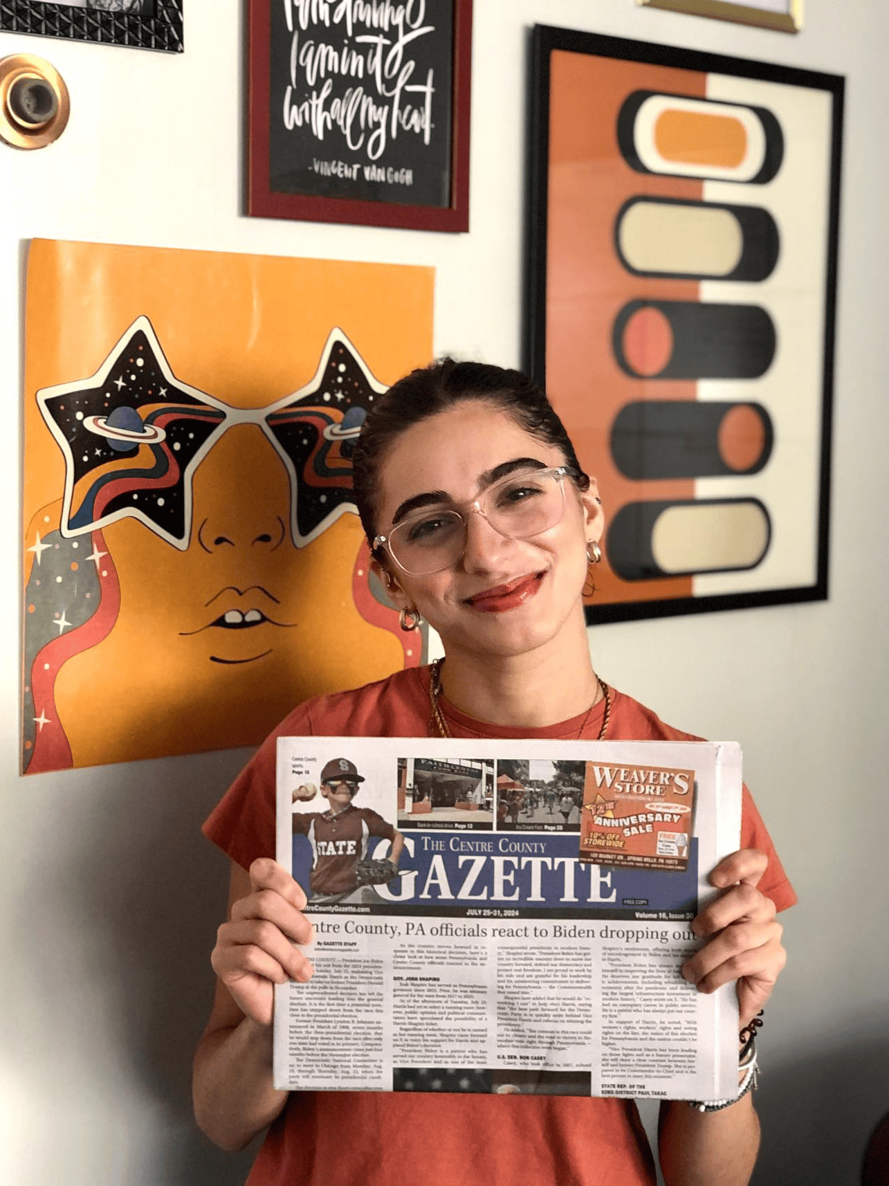 A student wearing glasses holds up an issue of the Gazette newspaper
