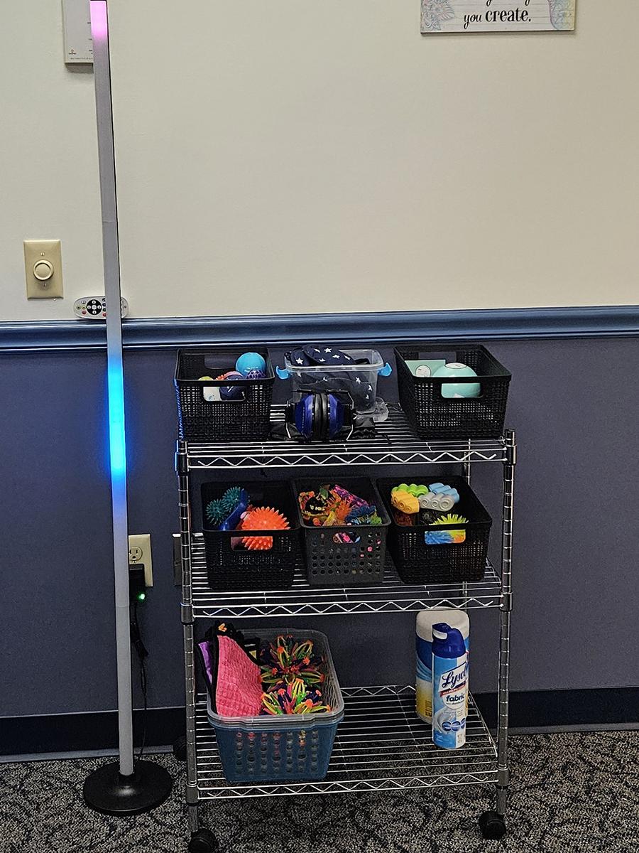 a tall, skinny light standing next to a small cart containing fidget spinners and sensory objects