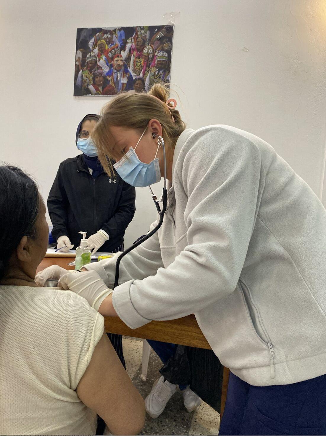 A woman wears a face mask while listening to a patient's heartbeat with a stethoscope