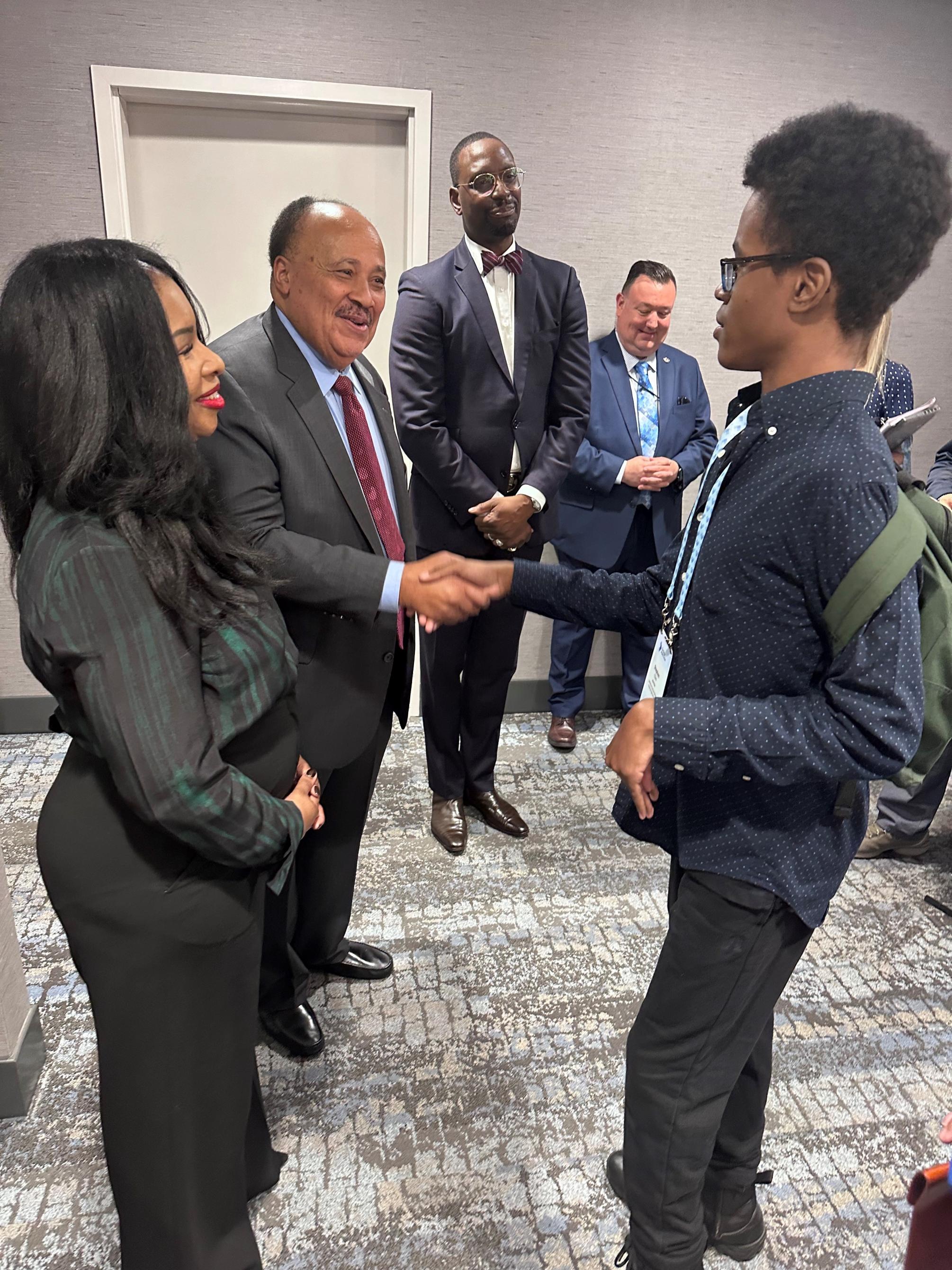 High school student shaking hands with a man at an event, other people onlooking