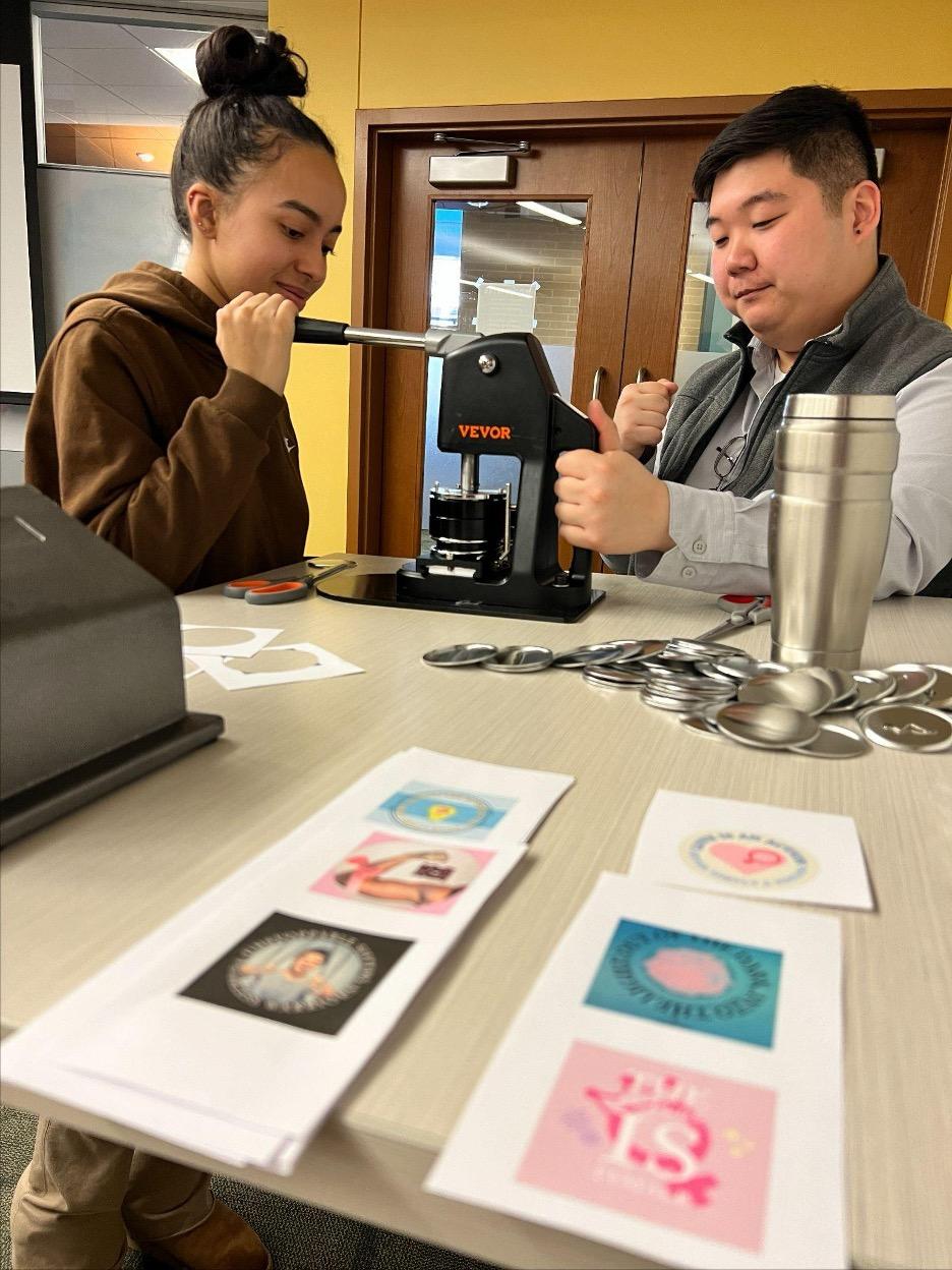 Maker Commons staff Chris Changjoon helps a WMNST106 student with their buitton project. 