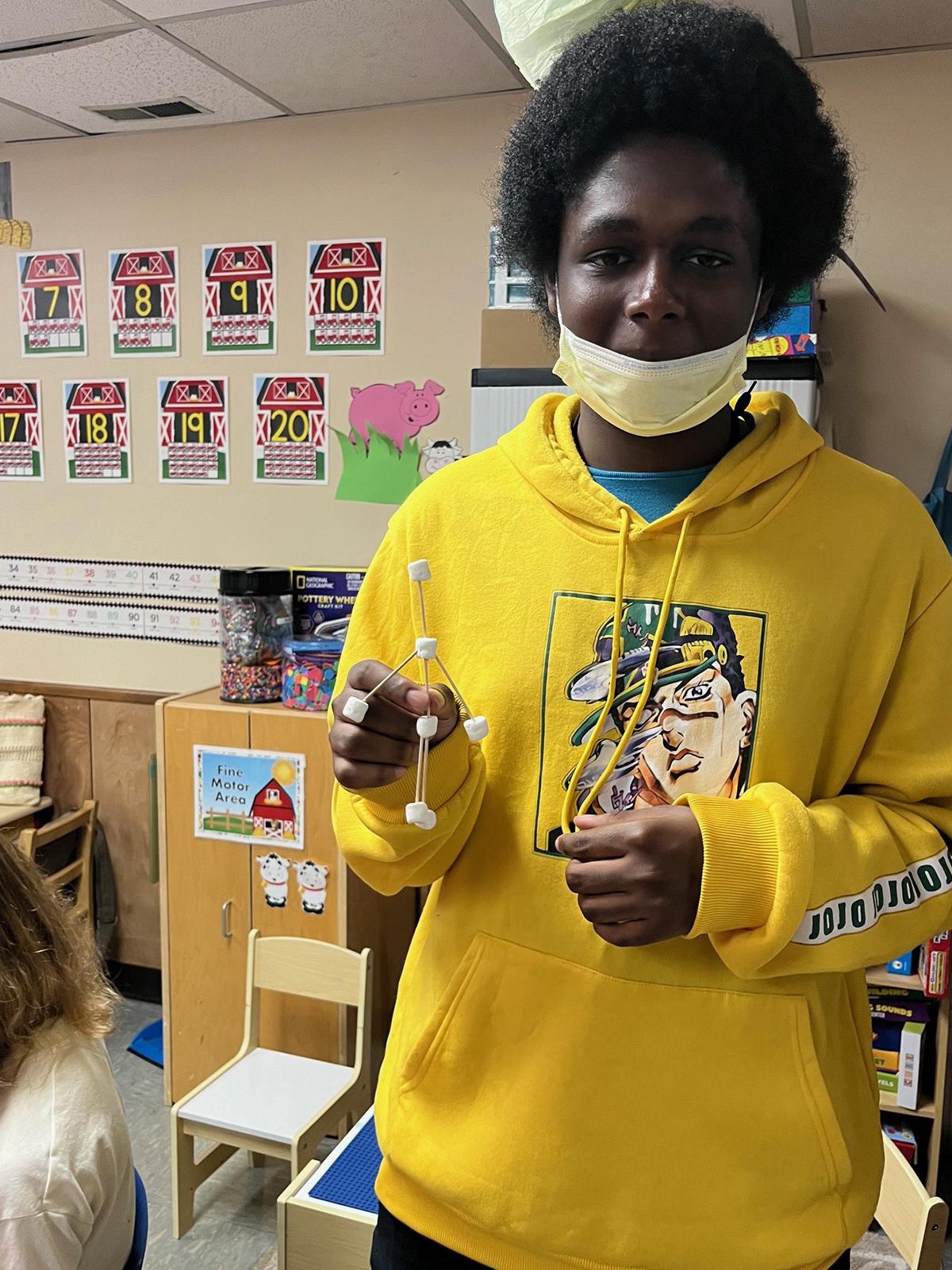 A high school student holding a science project in a classroom.