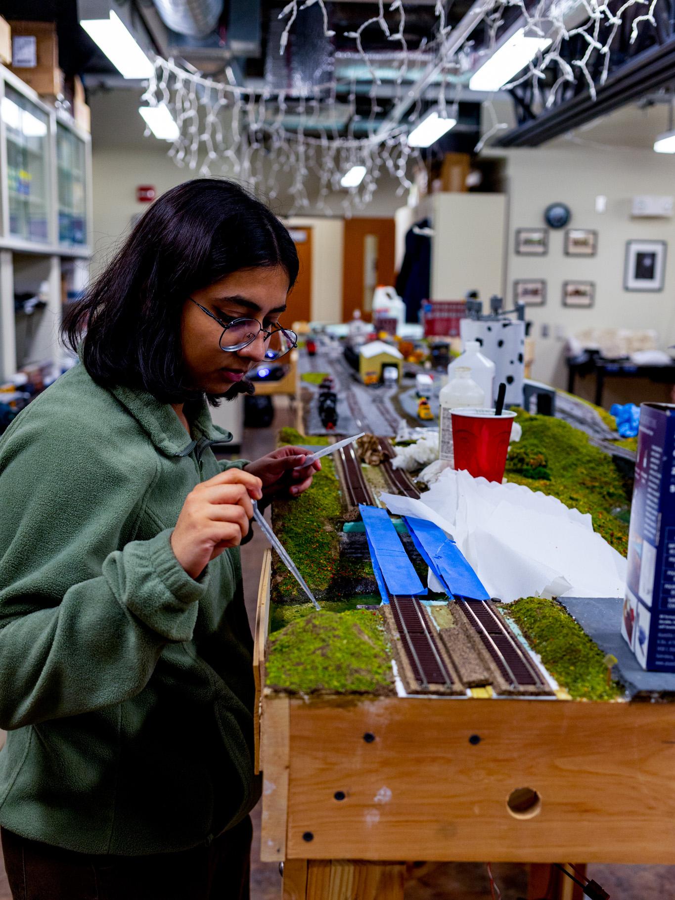 A student leans in close over a model railway with a pipette of glue
