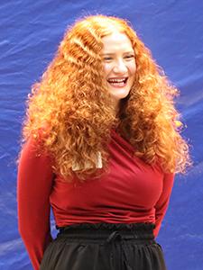 A woman smiles in front of a blue background.
