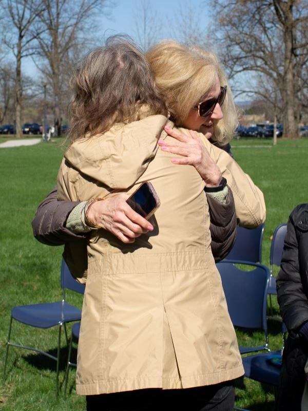 Two women hug on the Milton S. Hershey Medical Center campus. One woman is seen from behind, and the other woman is wearing sunglasses and holding a cell phone.