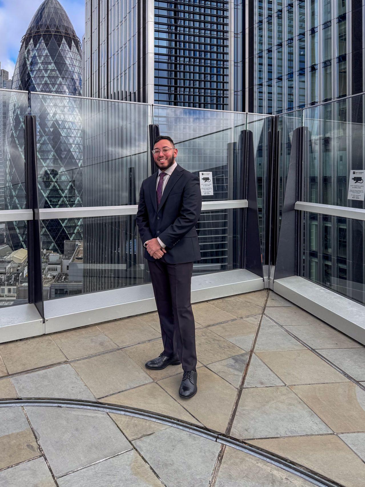A student wearing a suit stands on a rooftop in London