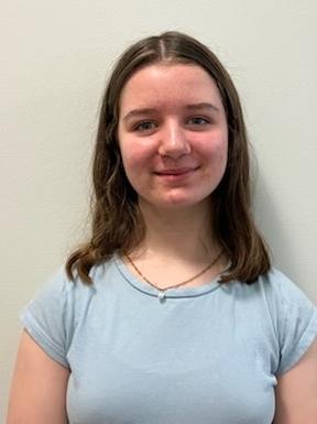 Seventh-grade student wearing a necklace and a blue shirt standing in front of a white backdrop