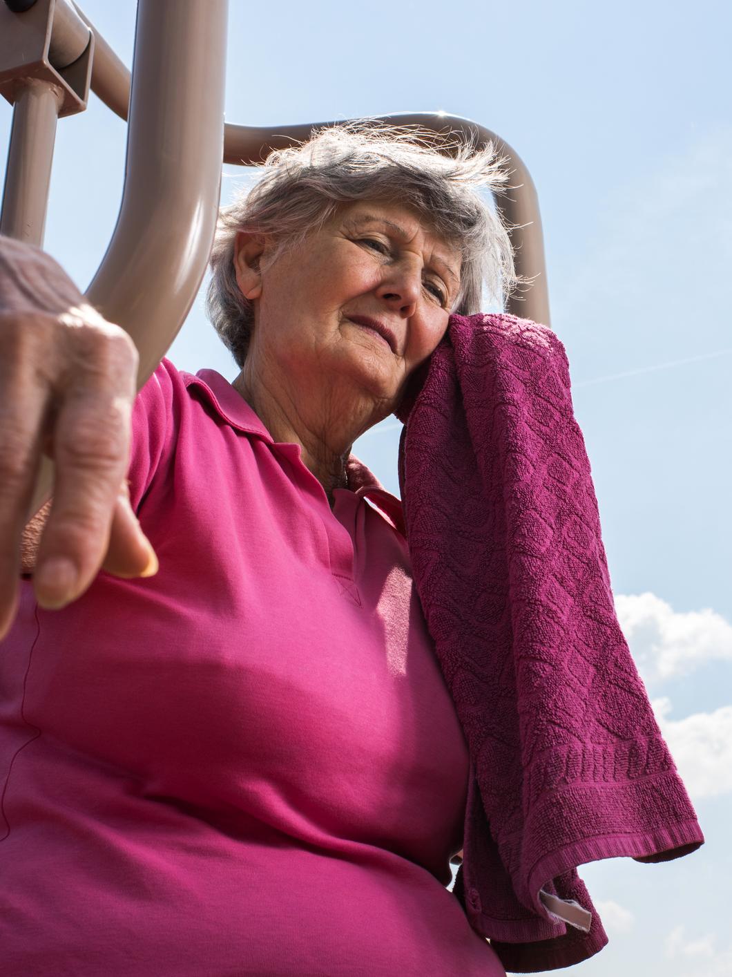 An older woman leans mops her brow in the sunshine