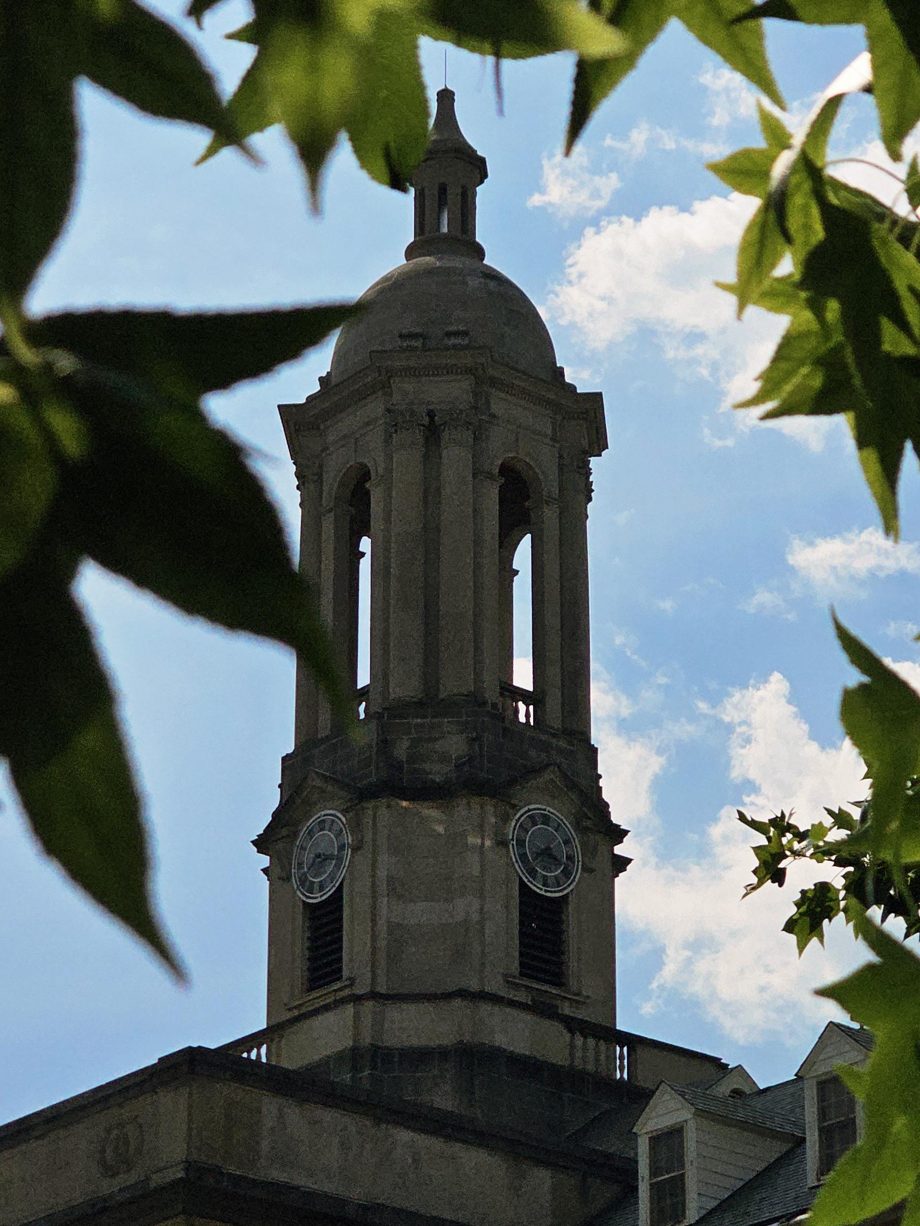 A close up of the Old Main bell tower framed by green leaves