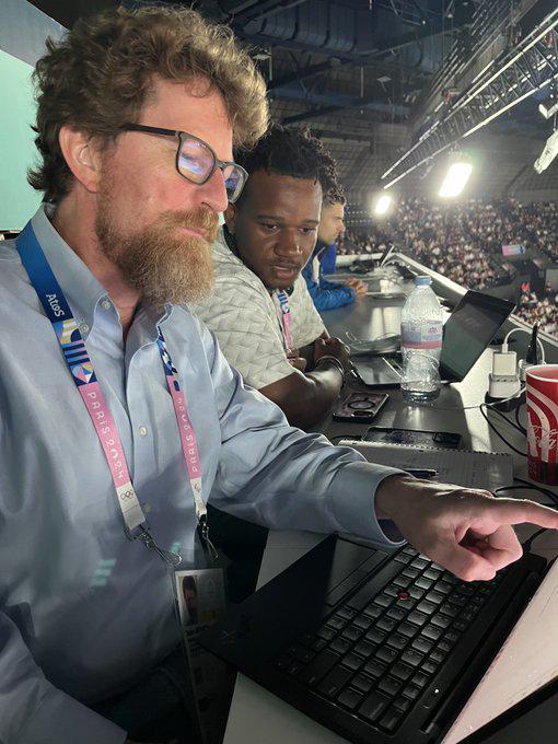 Bearded man in foreground left points out something on a computer screen to a student