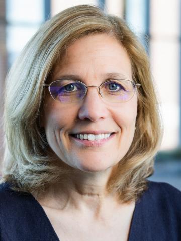 A woman with shoulder length hair and glasses looks into the camera smiling