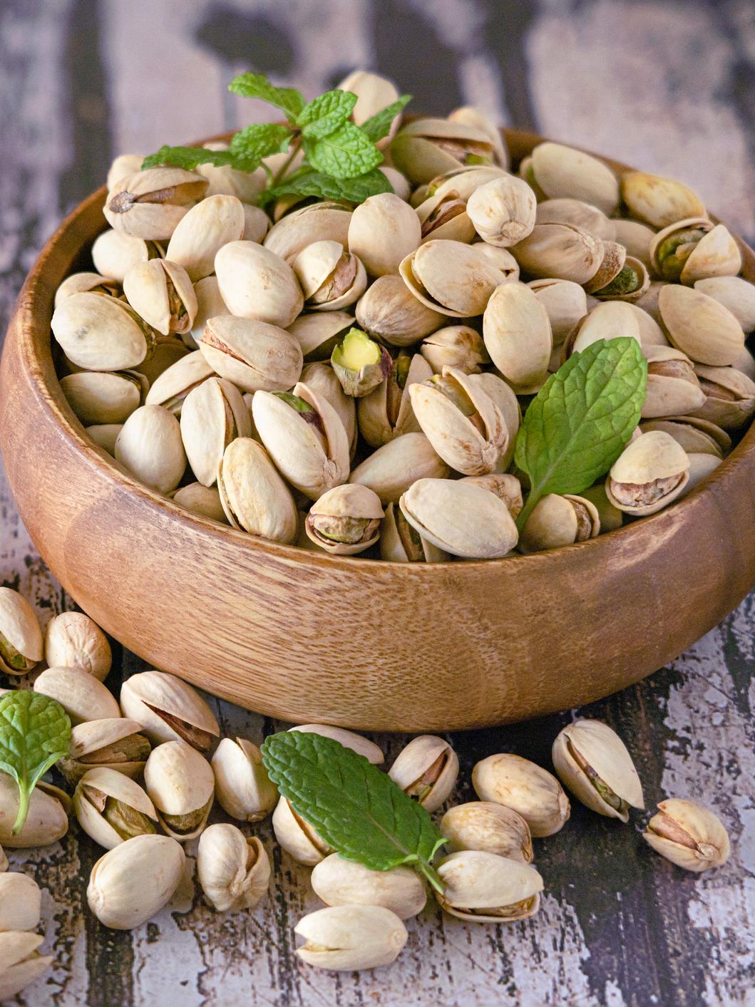 A small wooden bowl overflowing with pistachios and topped with sprigs of mint