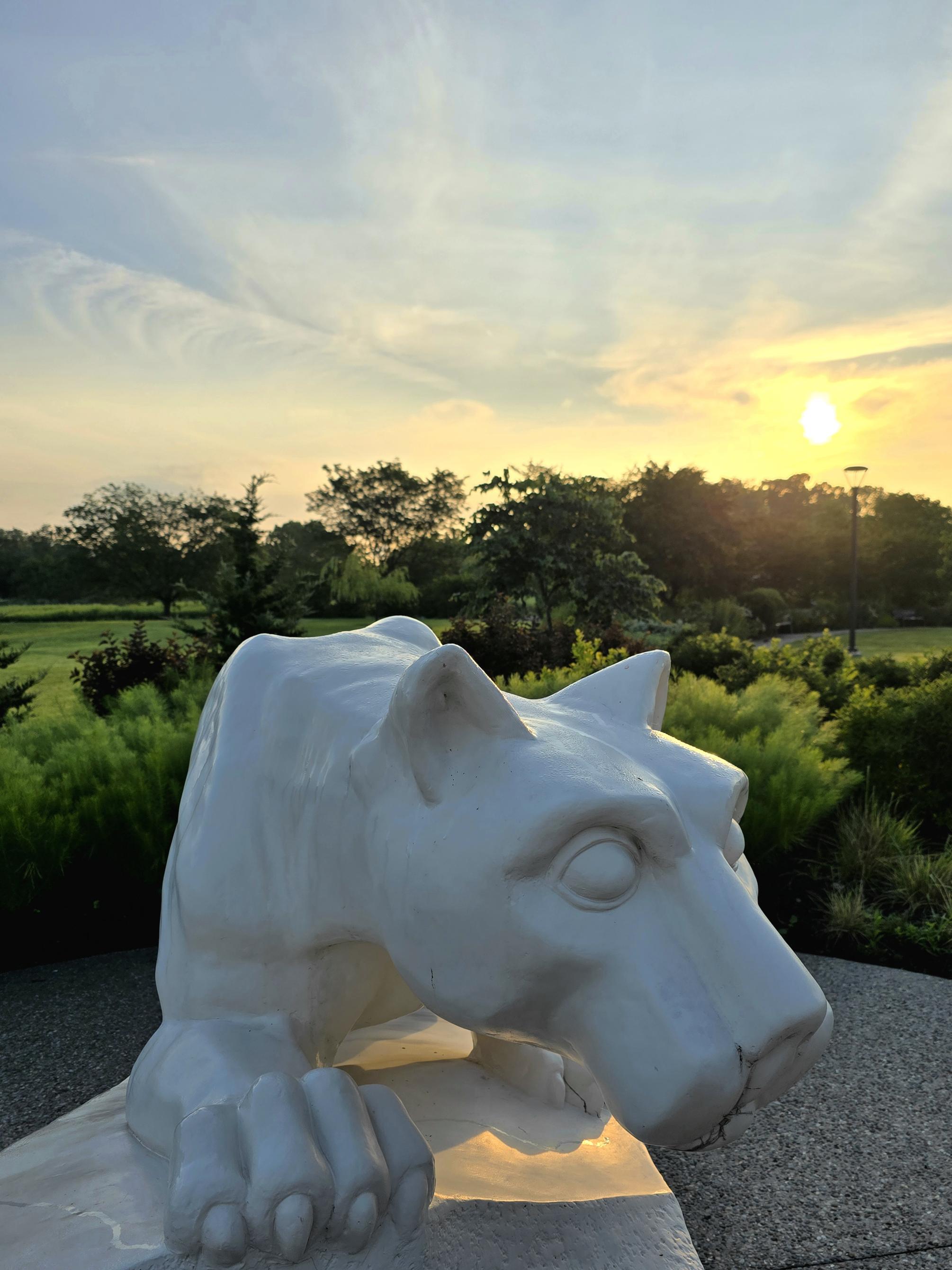 A close up shot of a Nittany Lion statue with the sunrise in the background