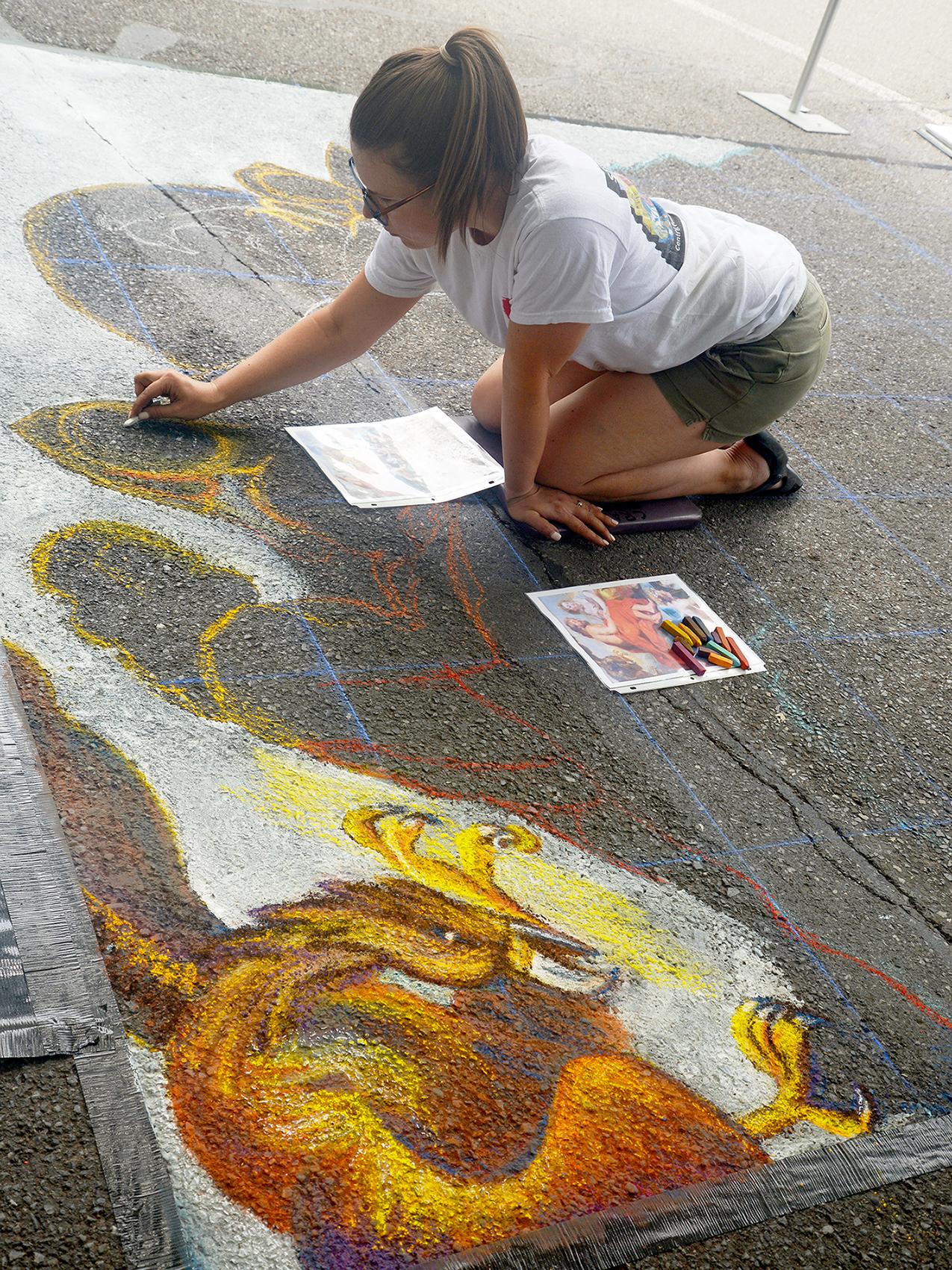 A person uses chalk on the street to create a colorful painting.